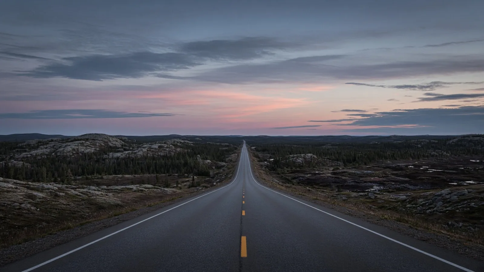 The two-lane paved ribbon of the Trans-Labrador Highway cutting straight across dark Canadian Shield rock and boreal spruce forest at twilight.