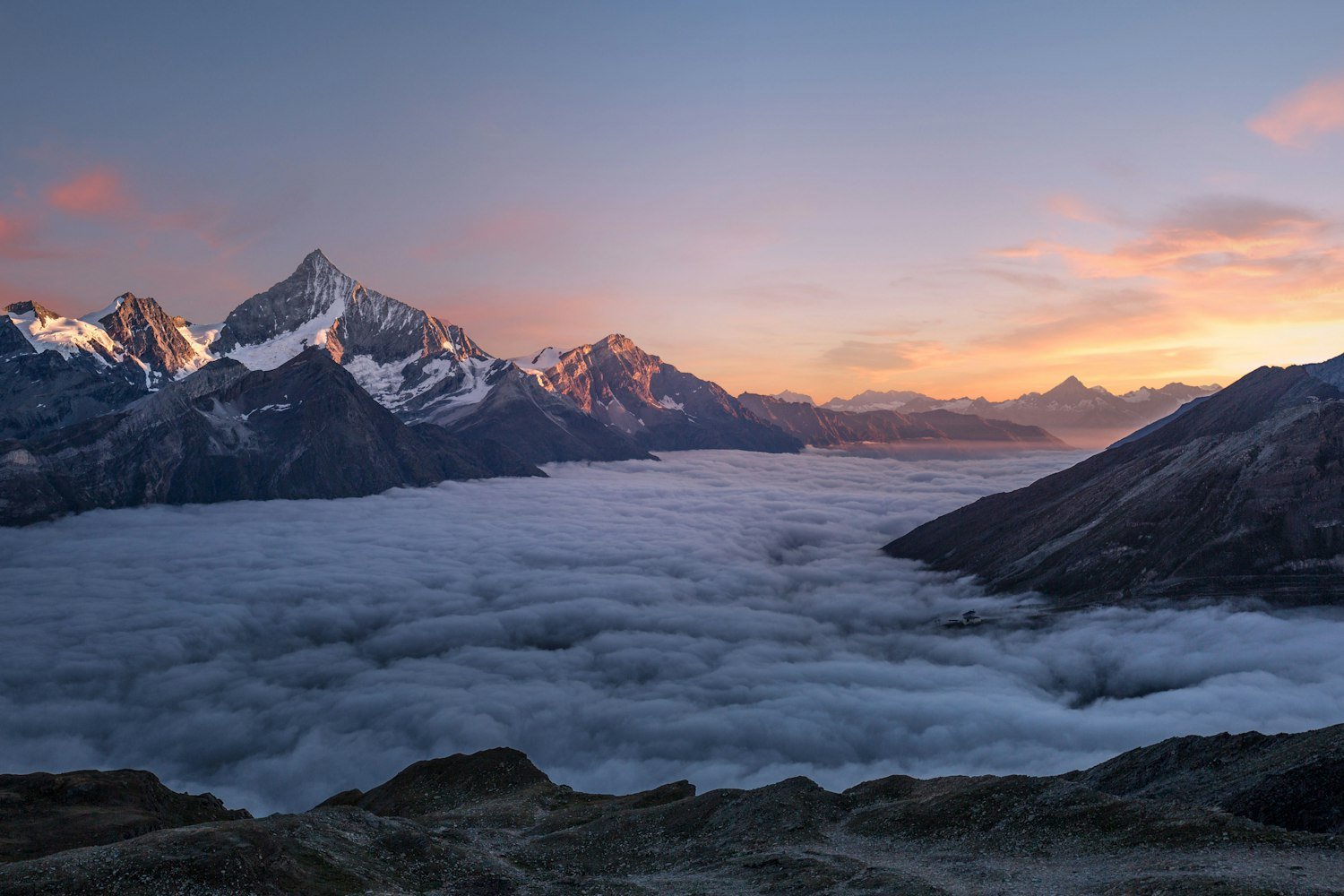 Snow peaks rising above a sea of cloud at dawn